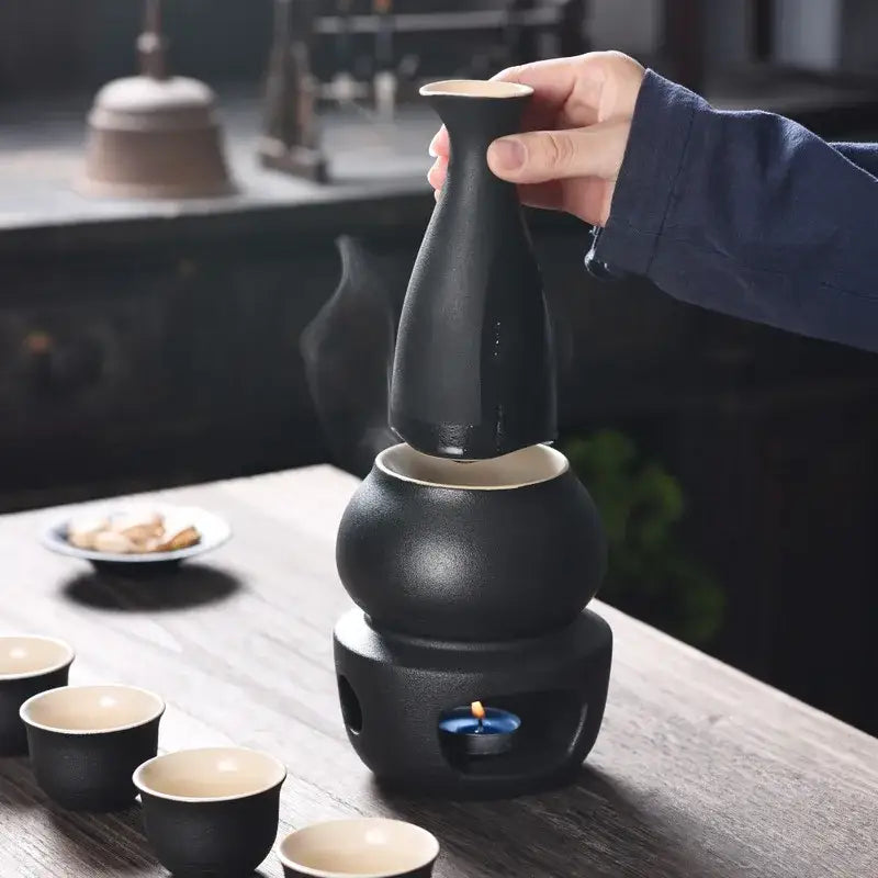 Matte black and light blue decorbites ceramic sake set with tall slender bottle and matching cups on wooden table