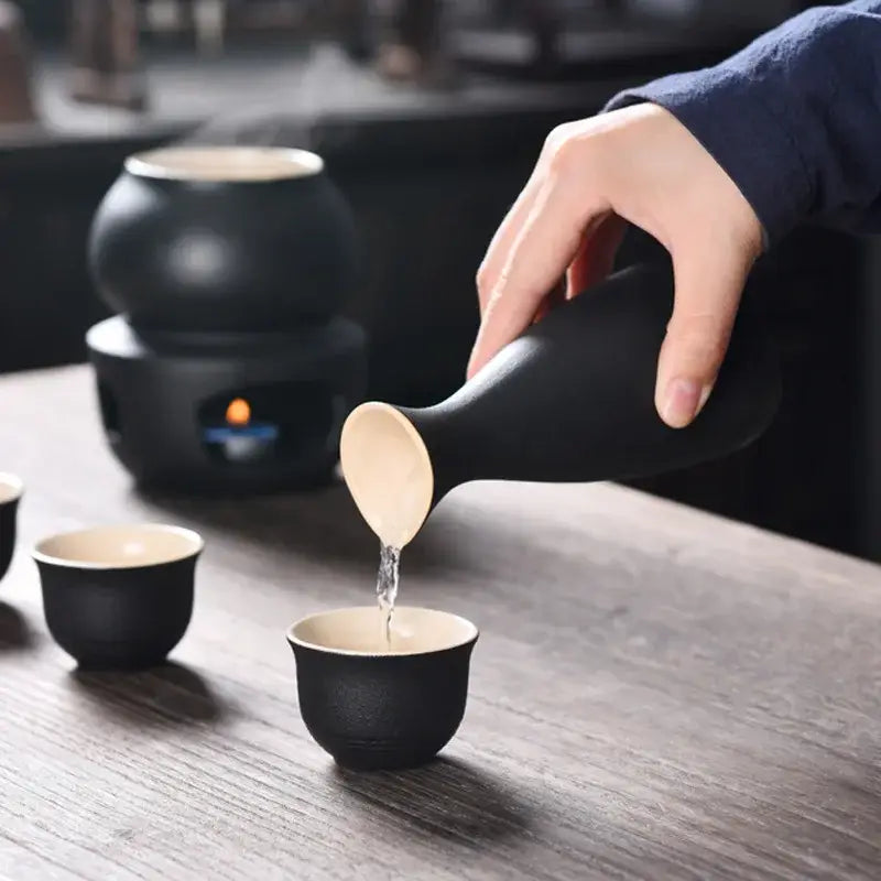 Matte black and light blue decorbites ceramic sake set with black ceramic decanter pouring into matching cups