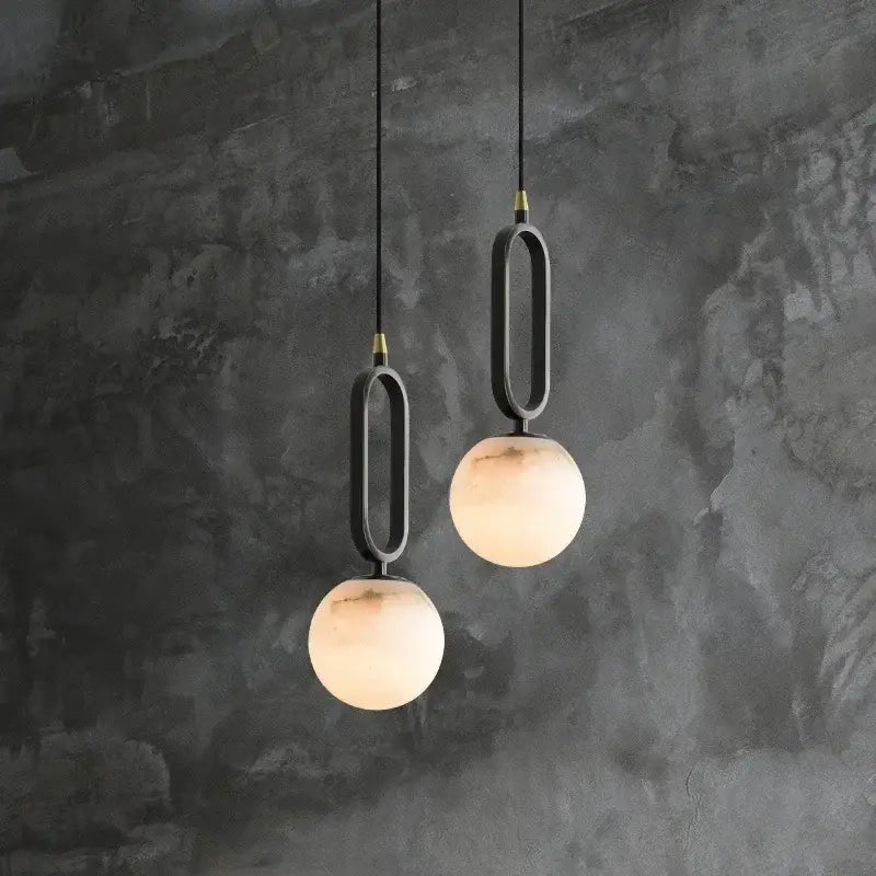 Two matte black pendant lights with frosted glass spheres and polished copper accents for dining room lighting