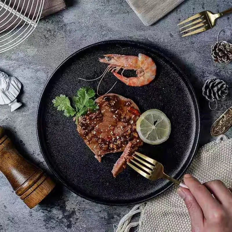 Matte black ceramic dinner plate with textured surface holding grilled steak with sauce cilantro lemon and shrimp decorbites black ceramic