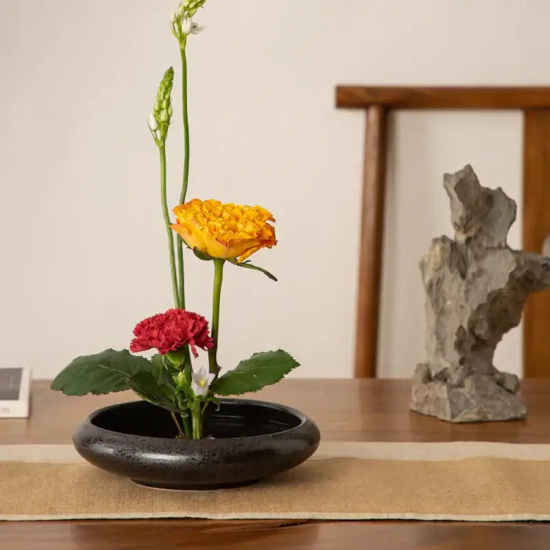 Matte black ceramic vase sword mountain set holding a minimalist floral arrangement with yellow and red flowers decorbites ceramic vase