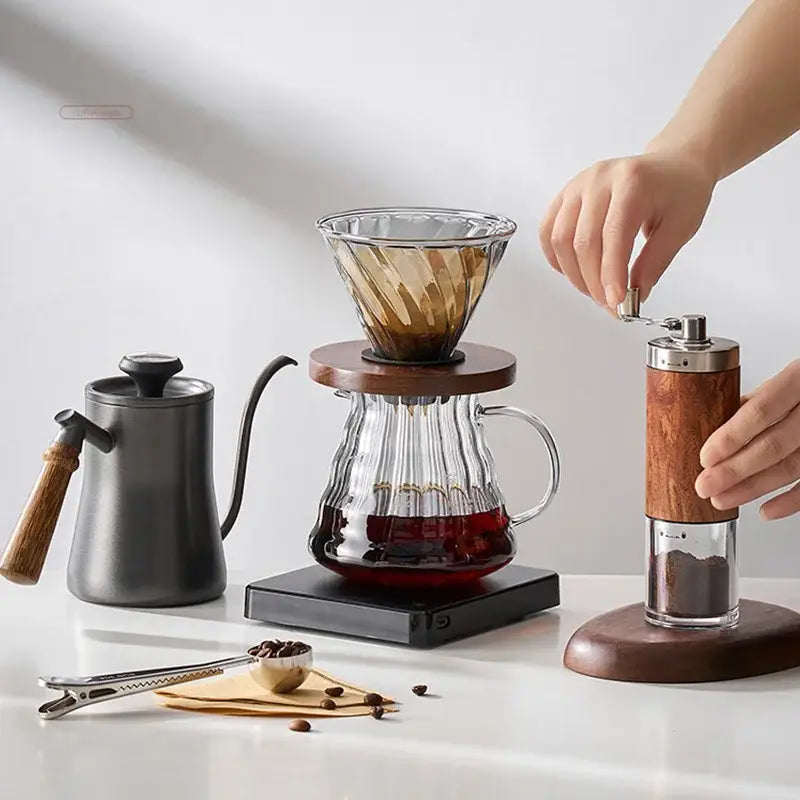 Glass coffee dripper with wooden base and gold-toned ribbed interior paired with matte black gooseneck spout kettle hand punch coffee pot
