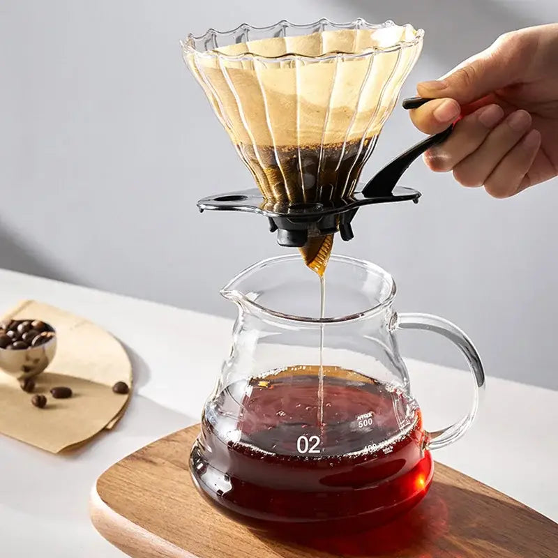 Clear glass pour-over coffee dripper with black clamp and paper filter filled with dark grounds paired with matte black gooseneck spout kettle hand punch coffee pot