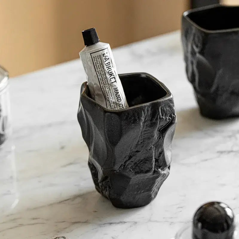 Matte black irregular shaped mouthwash cup made from silicone mold with a rough textured surface resembling cracked stone for bathroom use