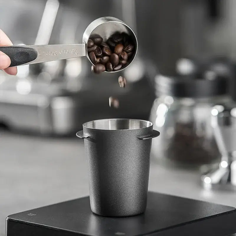 A sleek matte black stainless steel decorbites espresso dosing cup with textured handle measuring dark roast beans
