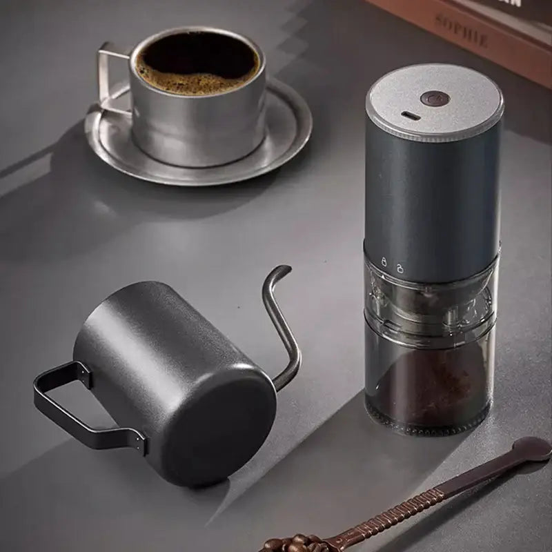 Matte dark teal electric coffee bean grinder with dark gray body, silver top cap, and clear glass chamber for grinding beans