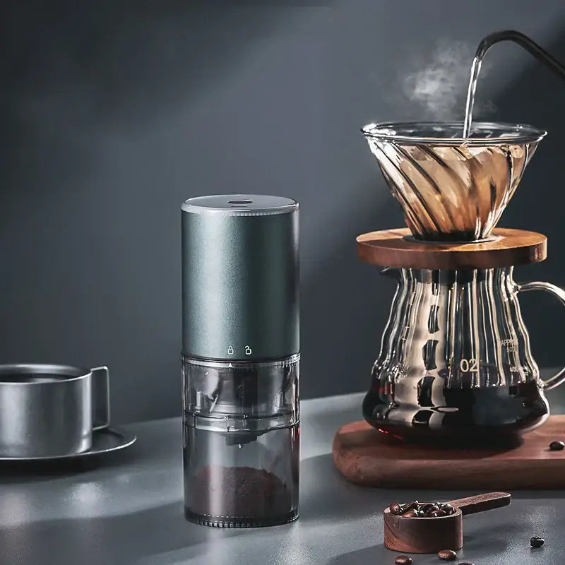 A sleek matte dark teal electric coffee bean grinder with a transparent chamber filled with ground beans