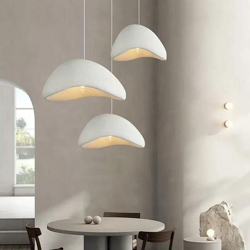 Three matte gray shell-shaped led wabi sabi chandelier pendant lights hanging in a dining room setting