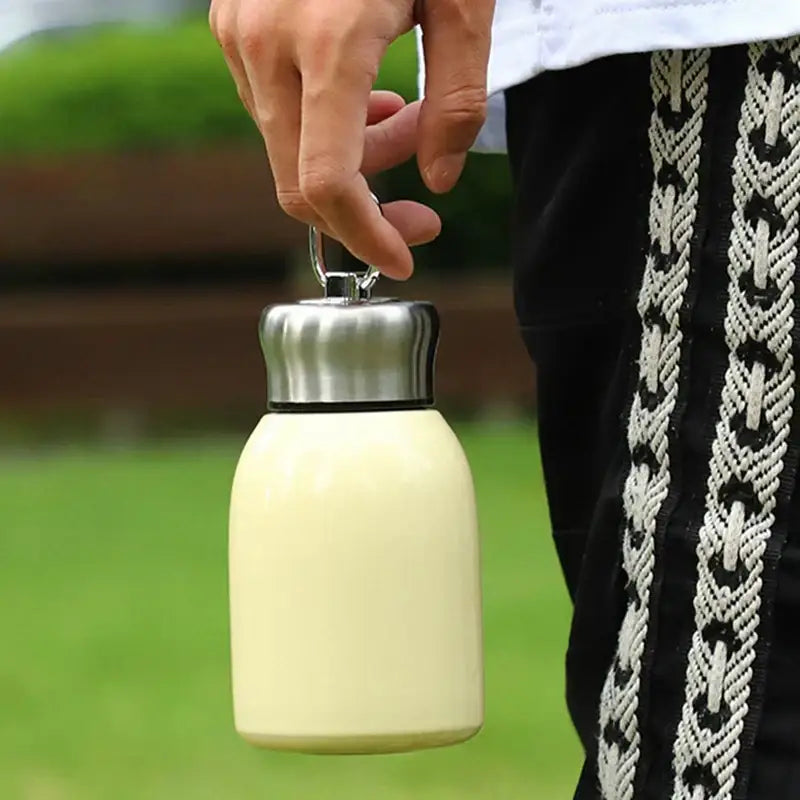Cream-colored stainless steel vacuum flask with silver lid and carrying loop for travel water bottle use