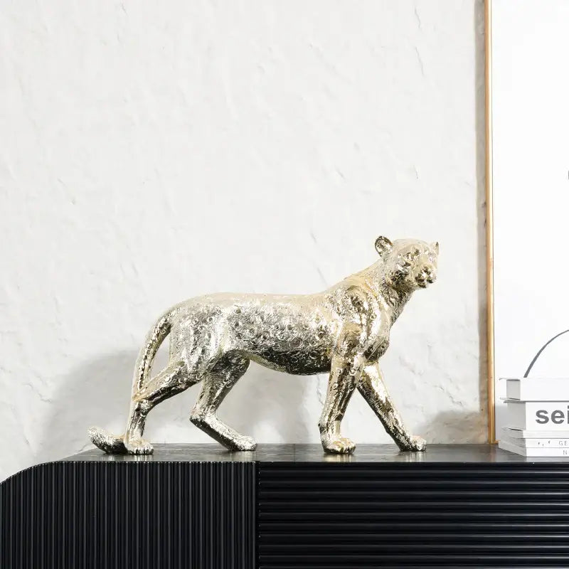 A sleek metallic gold decorbites leopard resin sculpture with textured surface on black ribbed shelf for living room decor