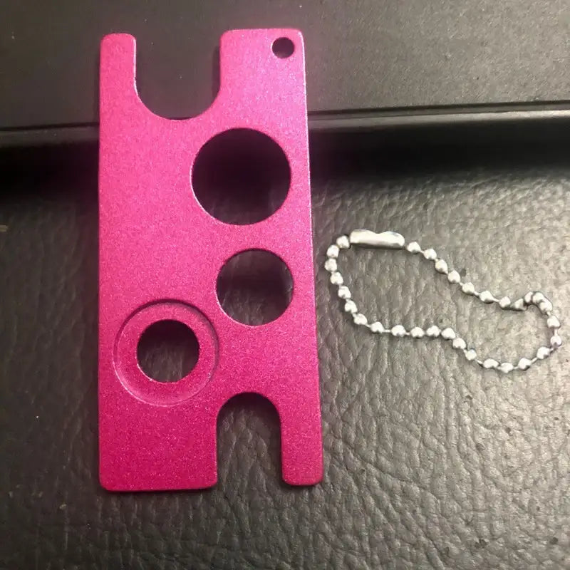 A vibrant pink metallic essential oils opener tool with circular and rectangular cutouts and a silver ball chain by decorbites essential oils