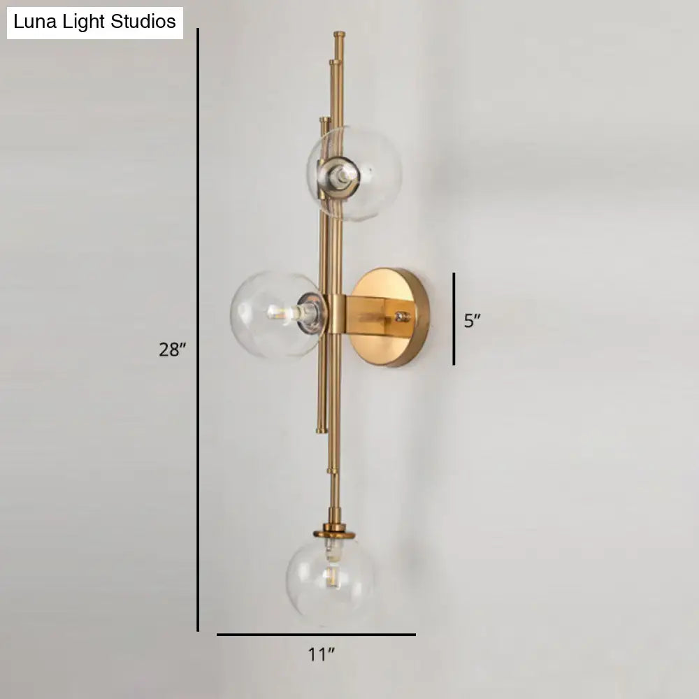 Mid century brass finish wall sconce with three clear glass orb shades and minimalist vertical fixture height design