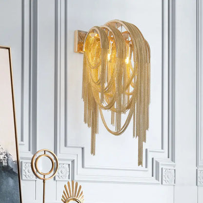 Gold-toned mid century wall lamp with silver stacked tassel chain links and modern sculptural design for bedroom sconce