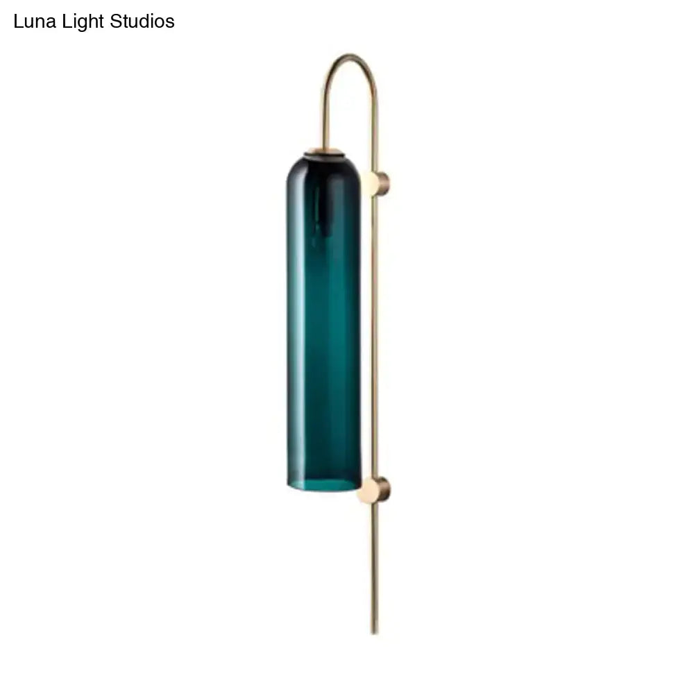 A mid century gooseneck wall light with a teal glass cylinder and brass arm for bedroom sconce lighting