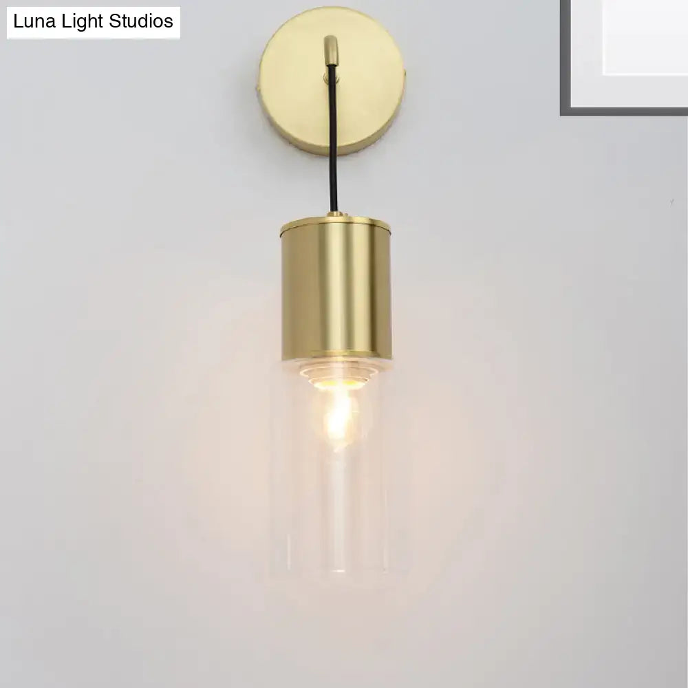 Minimal brass and glass wall sconce light with cylindrical design and exposed filament bulb for bedroom use