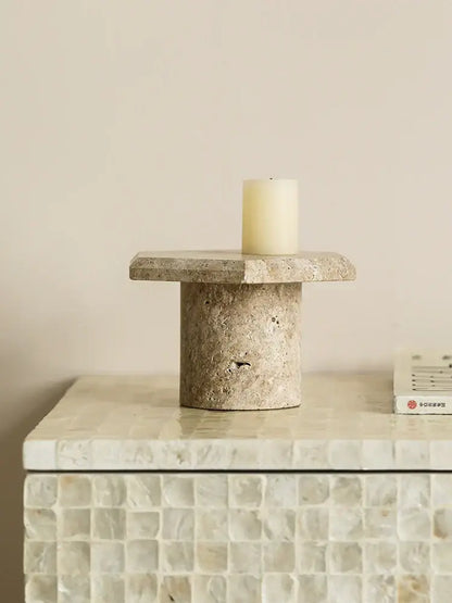 Beige brown travertine candle holder with cylindrical base and off-white pillar candle on minimalist serving tray