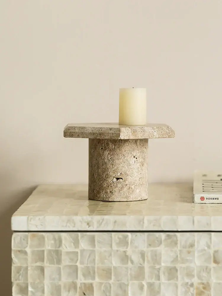 Beige brown travertine candle holder with cylindrical base and off-white pillar candle on minimalist serving tray