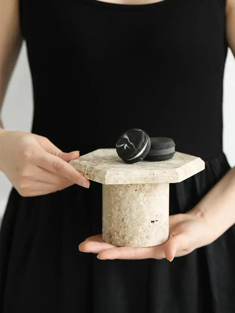 Beige brown travertine hexagon serving tray with a minimalist stone pedestal holding a black macaron