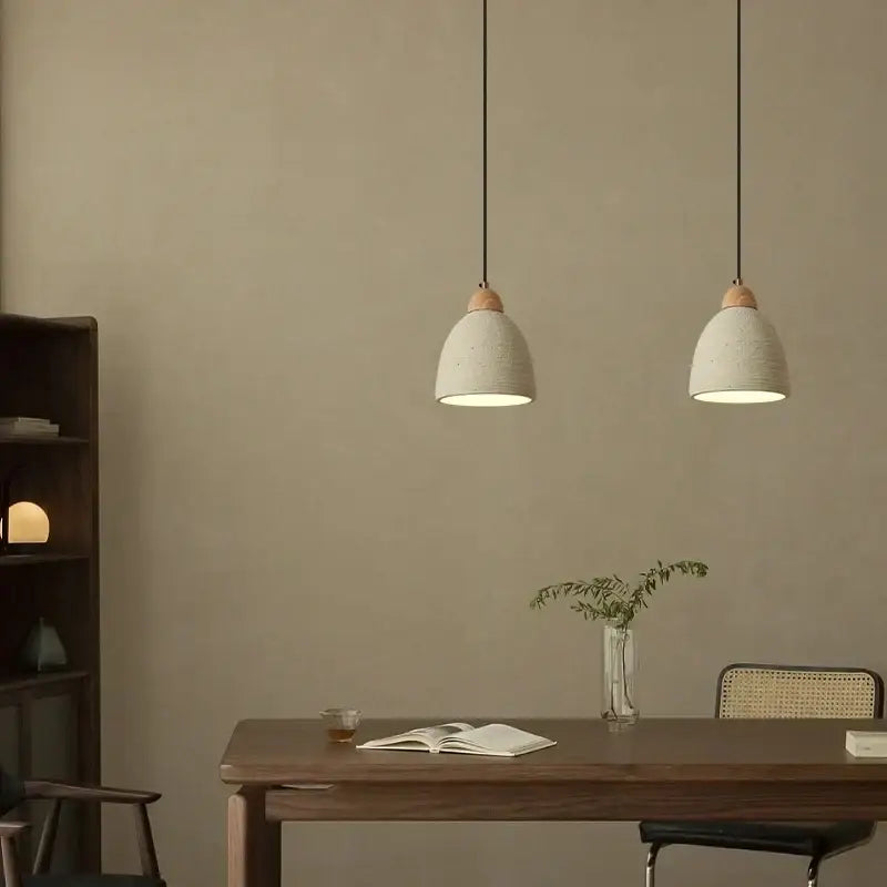 Two minimalist pendant lights with off-white ceramic shades and wooden accents by decorbites cement led hang above a table