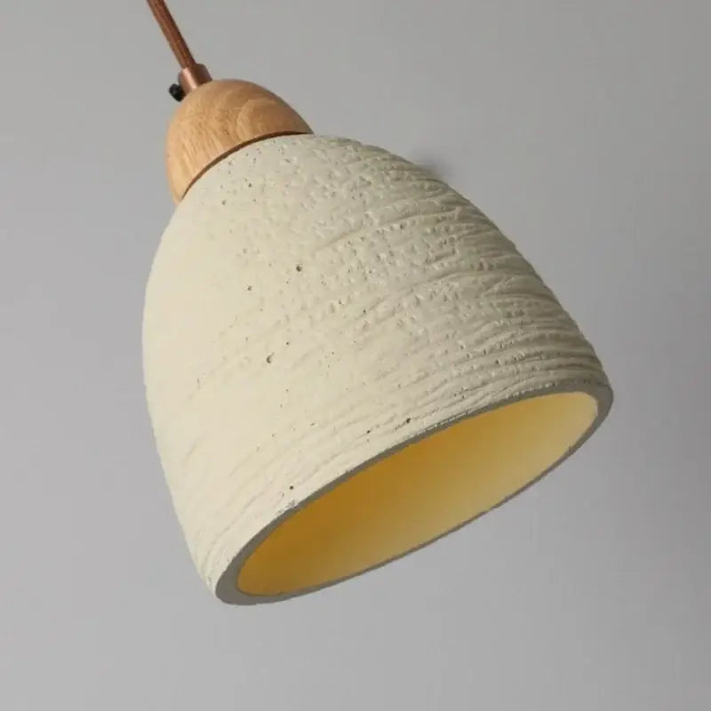 Cream-colored decorbites cement led pendant light with ribbed exterior, smooth yellow interior, and natural wood cap for kitchen decor