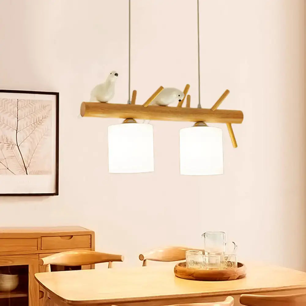 Beige drum island pendant lighting with two white cylindrical shades and decorative bird figurines on wood branch design