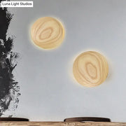Two minimalist beige wood circle wall sconces with natural grain and warm glowing led bulb parlor lights