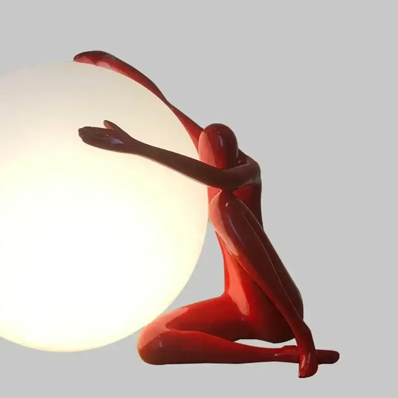 A glossy red decorbites humanoid sculpture led table lamp in a seated pose cradling a glowing spherical lamp