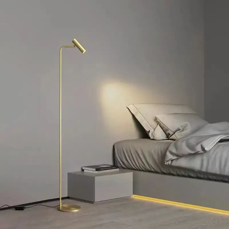 Gold-finished decorbites brass floor light with slender curved design and adjustable head for minimalist black bedroom decor