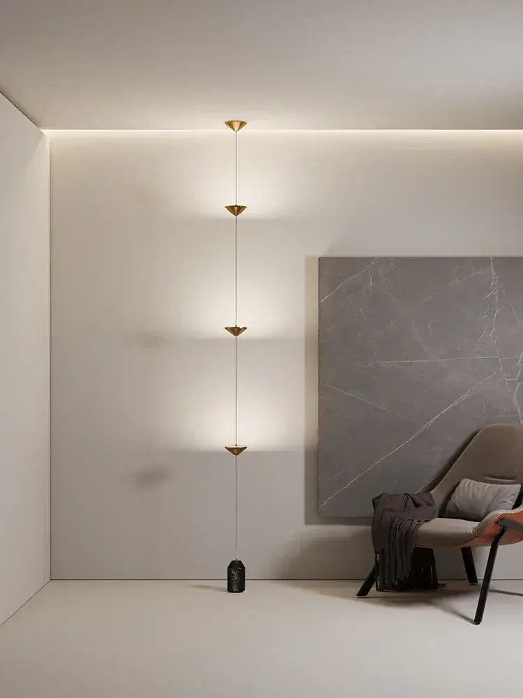 Minimalist black decorbites cone design floor lamp with gold-toned chain and four triangular lights on dark stone base