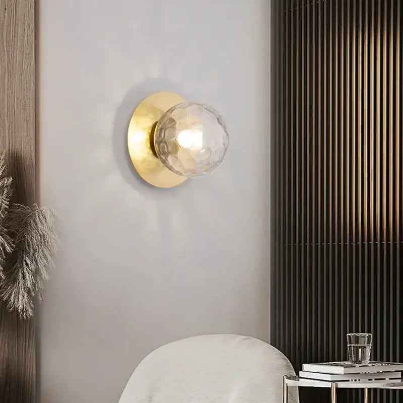Gold-toned led wall lamp featuring a minimalist black base and faceted clear glass globe for living room use