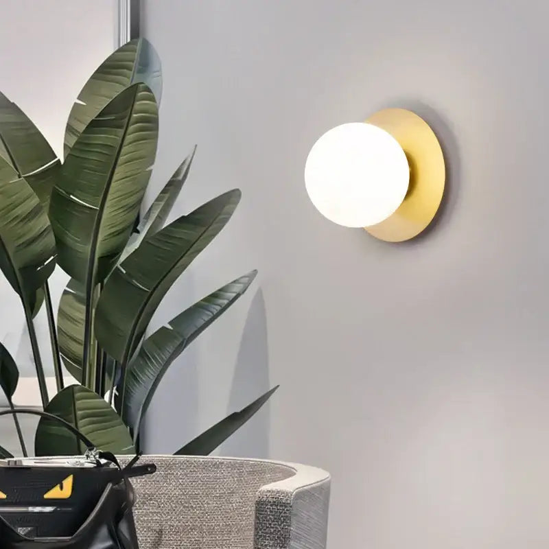 Gold-toned circular led wall sconce with frosted glass globe for minimalist black and gold bedroom lighting