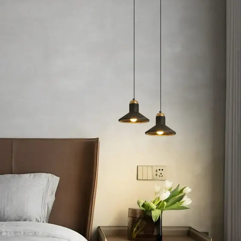 Two black travertine led pendant lights with brass accents hang above a bedside table for minimalist decorbites decor