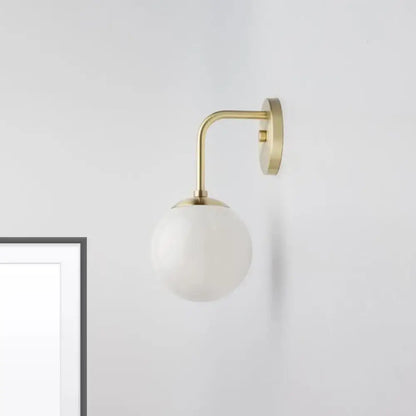 A minimalist golden black wall light with brass finish and a milky glass ball shade for bedroom lighting
