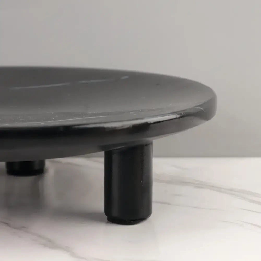 Black circular fruit tray with rounded edges and three short legs made of decorbites imitation marble for dining decor