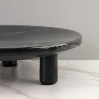 Black circular fruit tray with rounded edges and three short legs made of decorbites imitation marble for dining decor