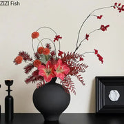 Minimalist black matte big belly ceramic vase holding vibrant artificial red and pink flowers with berry accents