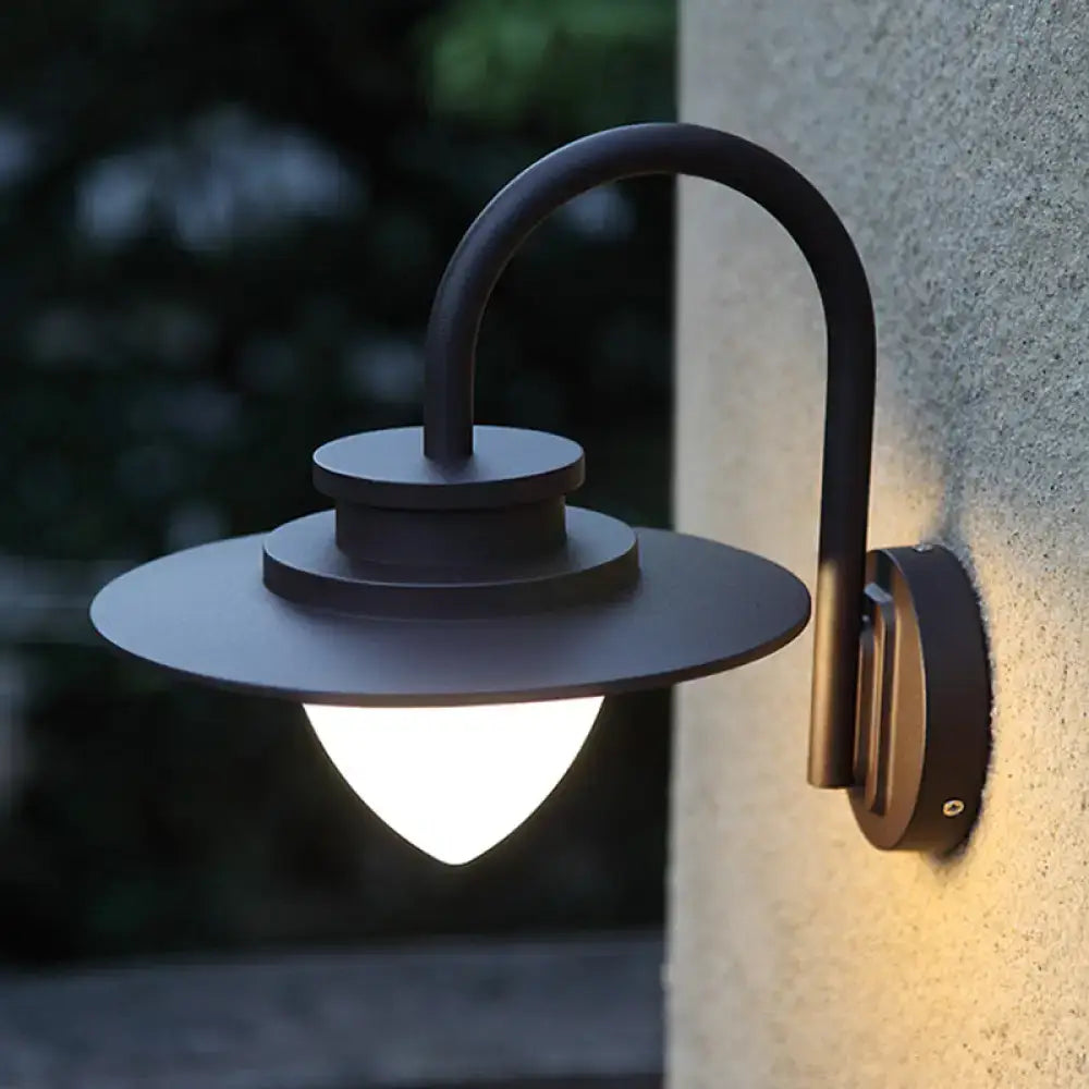Minimalist black metal outdoor wall sconce with curved arm and circular shade emitting warm light maximum bulb wattage 60w