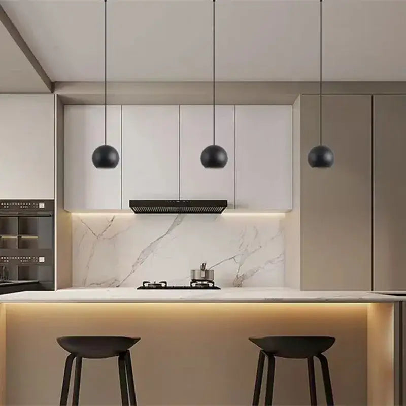 Three sleek black spherical die-cast aluminum pendant lights with acrylic lamp holders hang in a modern kitchen