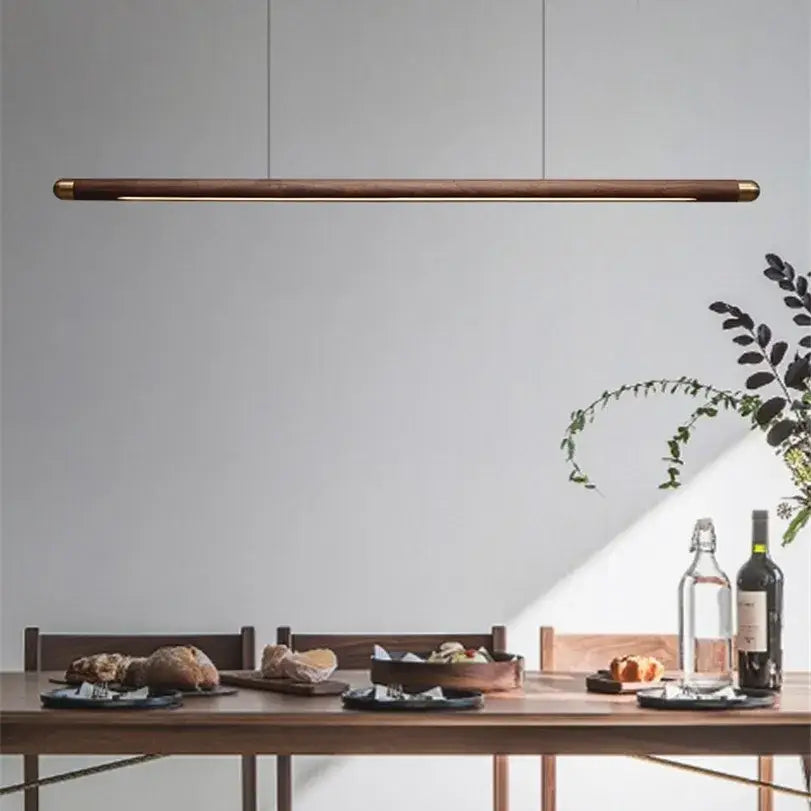 A minimalist black walnut wood pendant light with brass accents hangs above a dining table by decorbites