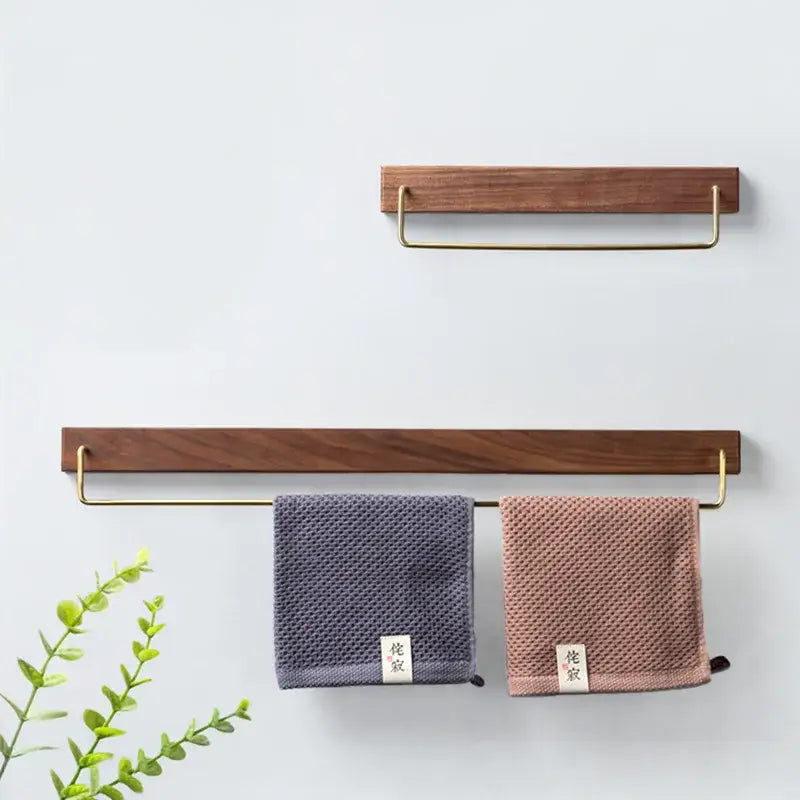 Two minimalist black walnut wood towel racks with brass handles holding muted gray and dusty rose microfiber towels