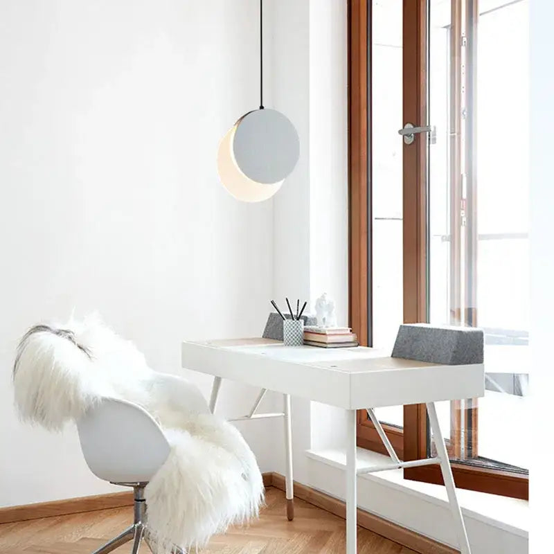 Minimalist white desk with slender metal legs below a black and white crescent moon pendant chandelier by decorbites
