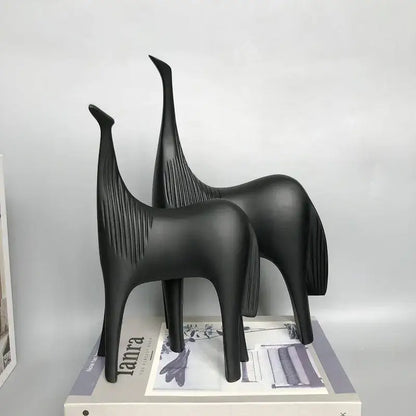 Two sleek matte black minimalist horse abstract ornaments with elongated necks and textured manes on a magazine for home decor