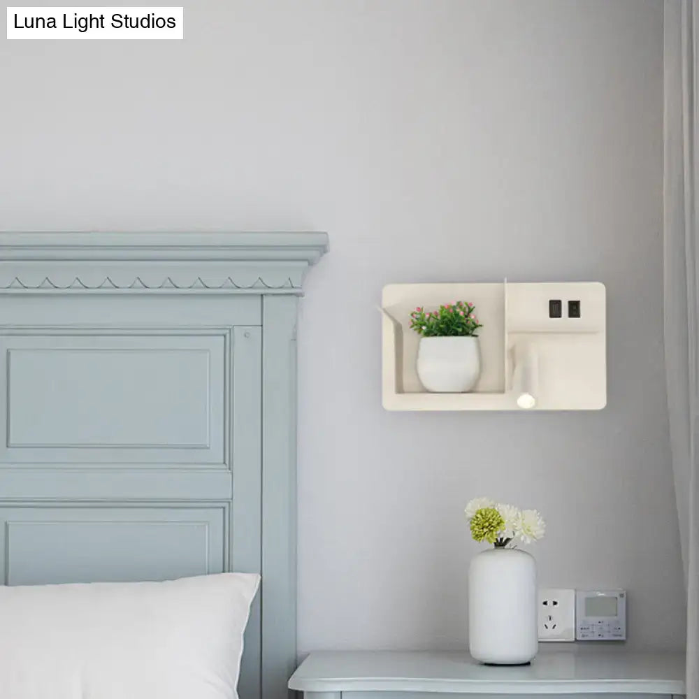 Minimalist black and white metal tubular wall light with bulb base, mounted above a white shelf with power outlets and plant