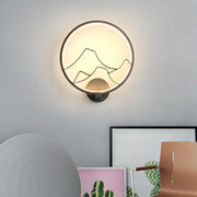 Minimalist black and white acrylic ring wall lamp with mountain silhouette and warm ambient light for bedroom use