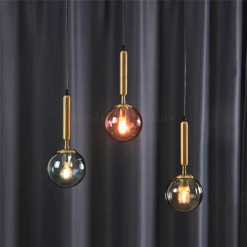 Minimalist blue pink and gray glass ball pendant light with brass accents hanging against dark curtain backdrop decorbites glass ball pendant