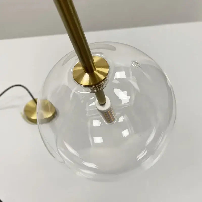 Minimalist pendant light with clear glass ball and brass-finished stem and base for dining room decorbites clear glass