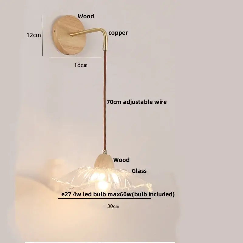 Minimalist brass wall light with a flower-shaped clear glass shade and warm glow mounted on wooden decorbites clear glass arm