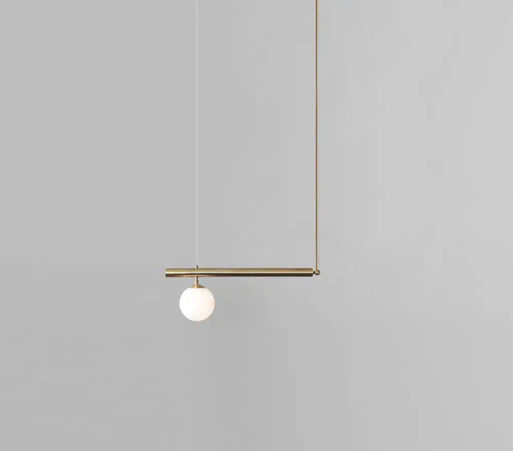 Minimalist brass ceiling light with a white glass globe suspended from a horizontal bar for kitchen island use