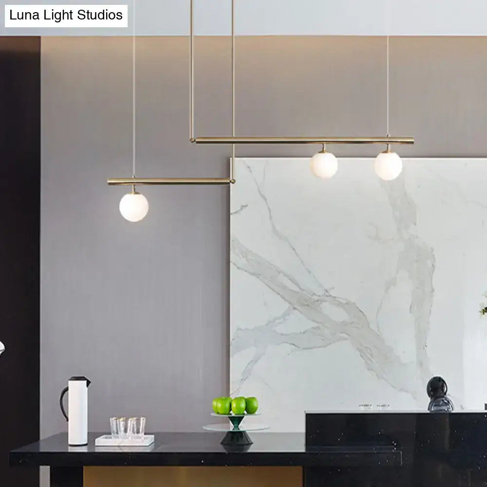 Minimalist brass ceiling light with three white glass globe bulbs suspended for kitchen island illumination