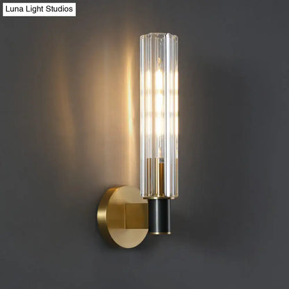 Minimalist tubular wall light sconce with a brass finish and clear vertically ribbed glass for bedroom use